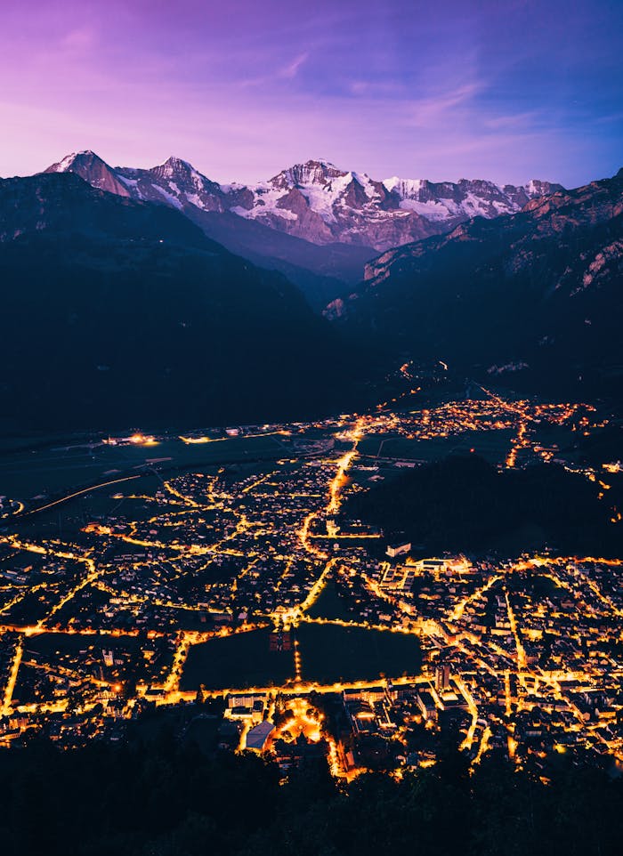 A mesmerizing aerial view of a beautifully lit town with majestic mountains in the twilight.